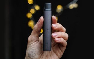 a person's hand holding a black logic vape device with yellow lights and black background