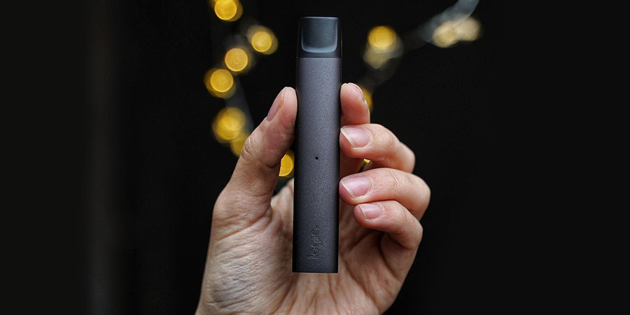 a person's hand holding a black logic vape device with yellow lights and black background